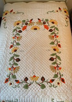 a white quilt with orange and yellow flowers in a circle on the edge of it