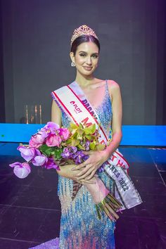 a woman in a blue dress holding flowers and a crown on top of her head