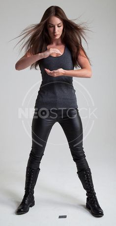 a woman with long hair standing in black leather pants and tight boots, holding her hands out