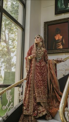 a woman in a red and gold bridal gown standing on the stairs with her arms outstretched