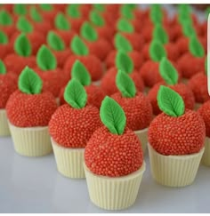 red cupcakes decorated with green leaves and sprinkles on a table