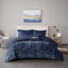 a bed with blue comforter and pillows in a room next to a painting on the wall