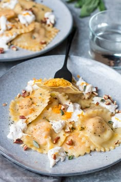 two plates filled with pasta and cheese on top of a table next to water glasses