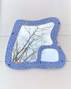 a blue mosaic mirror hanging on the side of a white wall with a tree in it