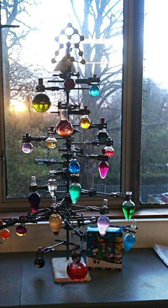 a christmas tree made out of different colored flasks in front of a window