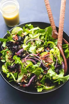 a salad with lettuce, onions and carrots in a black bowl next to a glass of orange juice