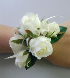 a wrist corsage with white roses and green leaves