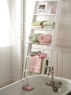 a white ladder shelf filled with towels next to a bathtub and sink in a bathroom