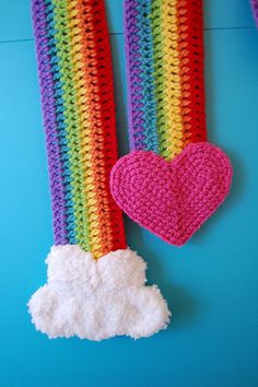 two crocheted hearts hanging from the side of a rainbow colored wall with clouds