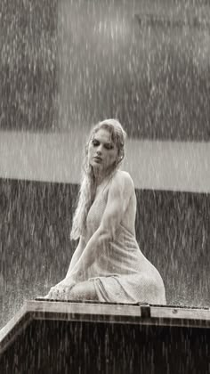 a woman sitting on top of a wooden bench in the rain