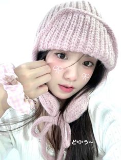 a young woman wearing a pink hat and scarf holding her hand to her ear while posing for the camera