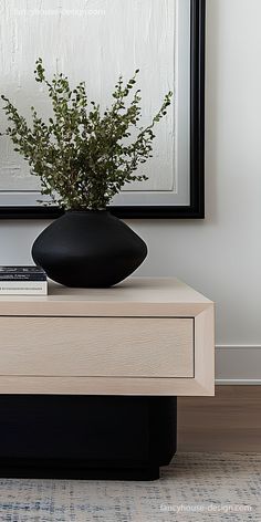 a black vase sitting on top of a wooden table next to a white framed painting