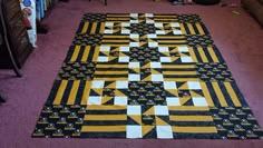 a large yellow and black quilt on the floor in a room with pink carpeting