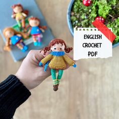 a hand holding a small doll next to a potted plant and a sign that says english crochet