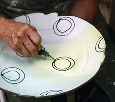 a person using a paintbrush to draw circles on a white plate with black ink