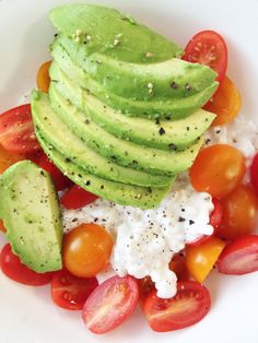 a white plate topped with sliced avocado, tomatoes and cottage cheese on top of rice