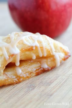 an apple pie with icing next to it on a wooden cutting board and two apples in the background