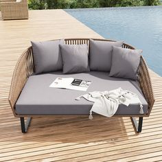 a wicker couch with grey cushions on a wooden deck next to a pool