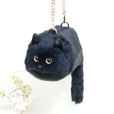 a black cat keychain hanging from a chain with flowers in front of it