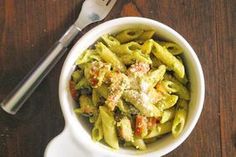 a white bowl filled with pasta on top of a wooden table next to a fork