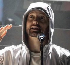 a man wearing a hoodie and holding his hands up in front of him while speaking into a microphone