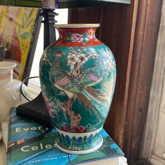 a vase sitting on top of a stack of books next to a lamp and other items