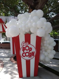 a popcorn box filled with white balloons sitting on top of a sidewalk next to a tree