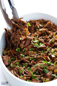 a white bowl filled with shredded beef and garnished with cilantro