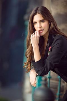 a woman leaning against a fence with her hand on her chin and looking at the camera