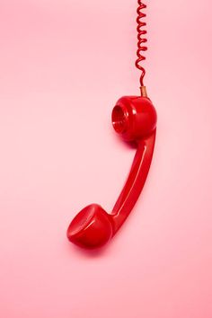 an old fashioned red telephone on a pink background with a cord attached to the phone