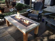 a fire pit sitting on top of a patio next to two chairs and a table