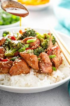 chicken and broccoli stir fry on top of white rice with chopsticks