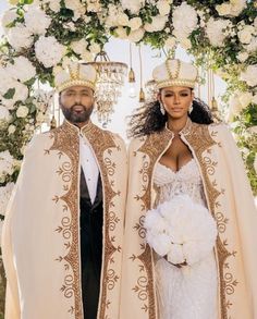 the newly married couple is dressed in white and gold outfits, standing next to each other