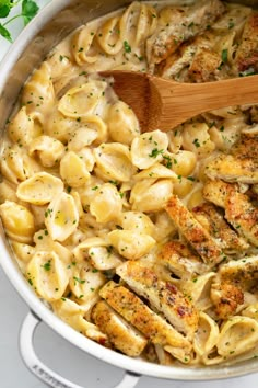 a pot full of chicken and pasta with a wooden spoon