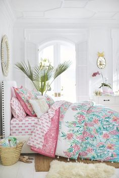 a bedroom with white walls and pink flowers on the bedspread, pillows and rugs