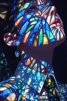 a woman's face is illuminated by the light from stained glass panels on her body