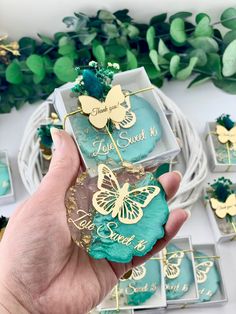 a person holding up some blue and gold butterflies on top of small boxes with green leaves in the background