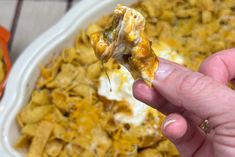 a hand holding a piece of food in front of a casserole dish