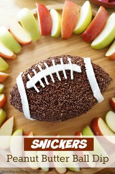 a football shaped cake with chocolate sprinkles and apples around it on a cutting board