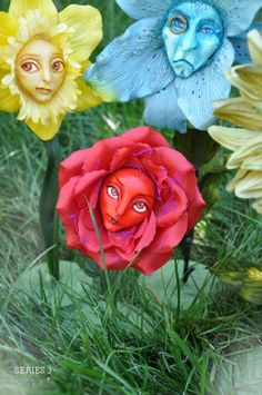 three colorful flowers with faces on them in the grass and one is painted like a human face