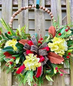 a wreath hanging on the side of a wooden fence with flowers and greenery around it