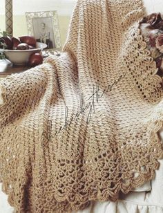 a crocheted blanket sitting on top of a bed next to a bowl of fruit