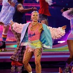 a woman in pink shirt and fishnet stockings on stage with other dancers behind her