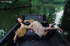 a woman laying on the back of a boat floating in a river surrounded by greenery