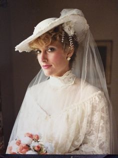 a woman wearing a white hat and veil with flowers on the bottom of her head