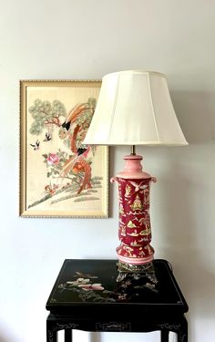 a lamp sitting on top of a black table next to a painting and framed artwork