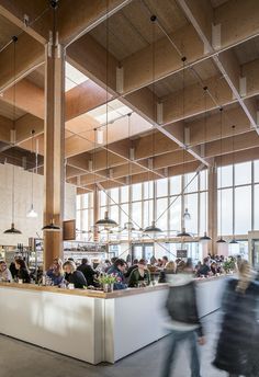 people are sitting at tables in a large room with lots of windows and wooden beams