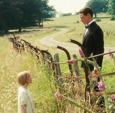 a man in a tuxedo standing next to a fence with flowers growing on it