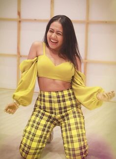 a woman in yellow top and plaid pants posing for the camera with her arms outstretched