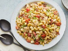 a white bowl filled with pasta salad next to two spoons on top of a table